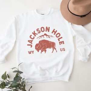 May include: White sweatshirt with a red graphic print of a buffalo, mountains, and the text "JACKSON HOLE WY US".