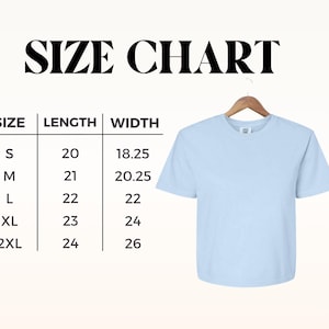 May include: A light blue t-shirt hangs on a wooden hanger. The image includes a size chart with measurements in inches for length and width, ranging from size small to 2XL. The text "SIZE CHART" is at the top.
