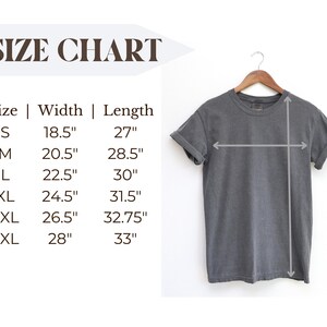May include: A gray t-shirt hanging on a wooden hanger, with a size chart displayed to the left. The size chart shows measurements in inches for sizes S through 3XL, including width and length.