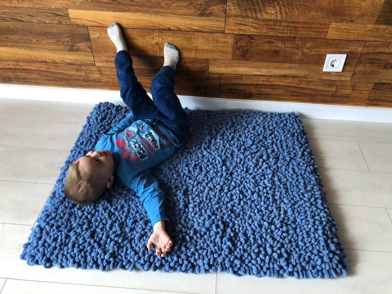 Peut inclure: Un tapis bleu touffu avec un enfant allong&eacute; dessus. Le tapis est rectangulaire et a une surface textur&eacute;e. L'enfant porte une chemise bleue &agrave; manches longues et un pantalon bleu.