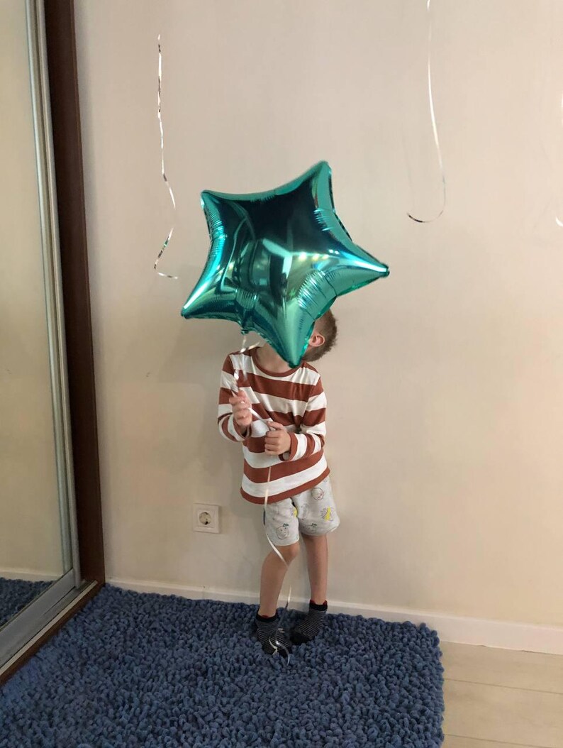 Peut inclure: Un ballon en forme d'&eacute;toile turquoise est tenu par une personne portant une chemise &agrave; manches longues ray&eacute;e et un short. Le ballon est brillant et refl&egrave;te la lumi&egrave;re. La personne se tient sur un tapis bleu.