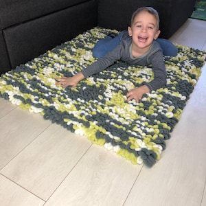 Peut inclure: Un tapis rectangulaire fait &agrave; la main avec un motif textur&eacute; en boucle. Le tapis pr&eacute;sente un m&eacute;lange de fils gris, blancs et vert clair. Le tapis est pos&eacute; sur un sol en bois de couleur claire.