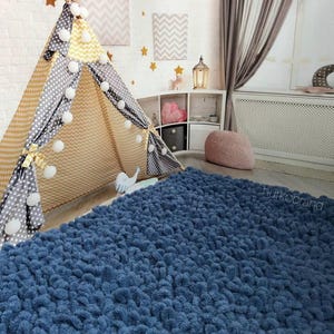 Peut inclure: Une chambre d'enfant confortable avec un tapis bleu textur&eacute;, un tipi avec des motifs jaunes et gris, et des &eacute;toiles d&eacute;coratives sur le mur en briques blanches. La pi&egrave;ce comprend une petite &eacute;tag&egrave;re avec des jouets et un pouf rose.
