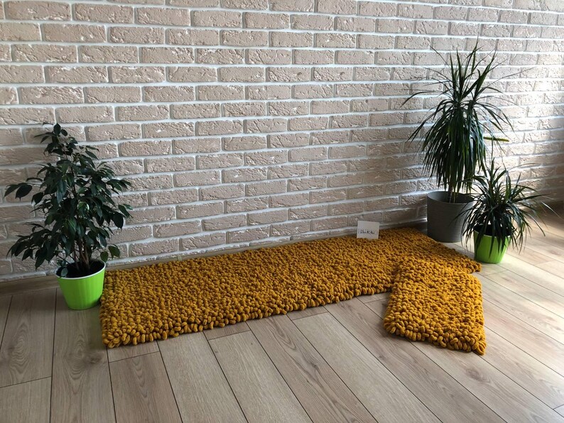 Peut inclure: Ensemble de tapis en tricot &eacute;pais jaune moutarde. L'ensemble comprend un long tapis rectangulaire et un plus petit tapis carr&eacute;. Les tapis sont pos&eacute;s sur un plancher en bois clair, avec des plantes en pot et un mur de briques en arri&egrave;re-plan.