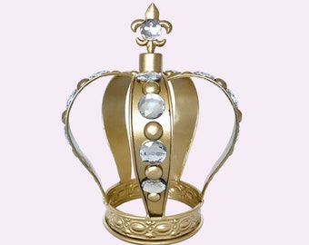 May include: A gold crown with clear rhinestones and a fleur-de-lis design on top.