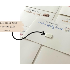 May include: A set of white cards with handwritten messages for different occasions. The cards have text that reads "for when you want to eat out", "for when you need a study break", and "for when you need new clothes". A small piece of double-sided tape is shown to attach the cards to gifts.
