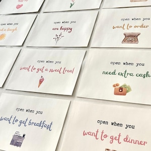 May include: A set of 10 white envelopes with colorful illustrations and text that reads "open when you..."  The text includes phrases like "need a laugh", "are happy", "want to order in", "need coffee", "want to get a sweet treat", "want to get breakfast", "need extra cash", and "want to get dinner".