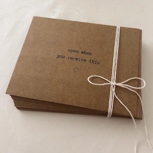May include: A stack of brown envelopes tied with a white string. The top envelope has the text "open when you receive this" and a small heart symbol.