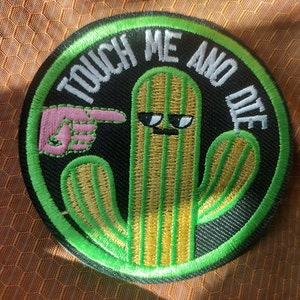 May include: A green and yellow embroidered cactus patch with a pink pointing finger and the text "Touch Me And Die".