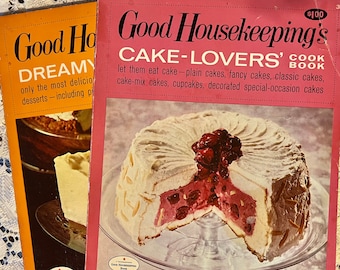 May include: Two vintage Good Housekeeping cookbooks. The cover of the red cookbook features a cake with a cherry topping and the text "Good Housekeeping's Cake-Lovers' Cook Book". The cover of the orange cookbook features the text "Good Housekeeping's Dreamy" and a picture of a dessert.