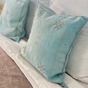 May include: A bed with a brown blanket and white pillows. Two blue patterned throw pillows are on top of the white pillows.