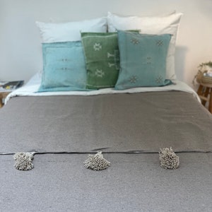 May include: A grey bed with a grey throw blanket with white pom-poms. The bed has white and blue patterned pillows and a green patterned pillow.