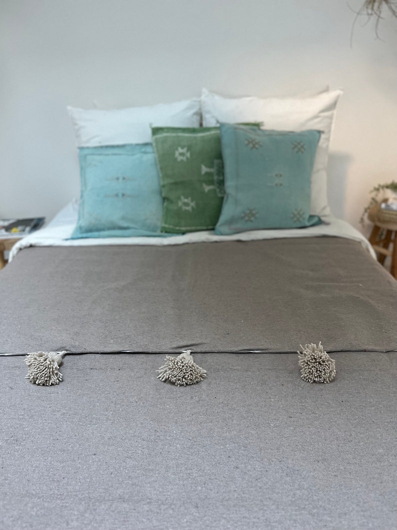 May include: A grey bed with a grey throw blanket with white pom-poms. The bed has white and blue patterned pillows and a green patterned pillow.