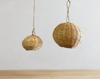 May include: Two round, woven, hanging light fixtures made of natural materials. The larger fixture is hanging in front of the smaller fixture.
