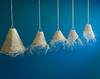 May include: Six woven pendant lights with frayed edges hang from the ceiling against a blue wall. The lights are different sizes and are all made of natural materials.