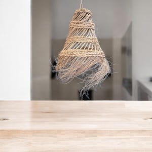 May include: A woven light fixture with a natural, straw-like texture hangs above a light wood table.