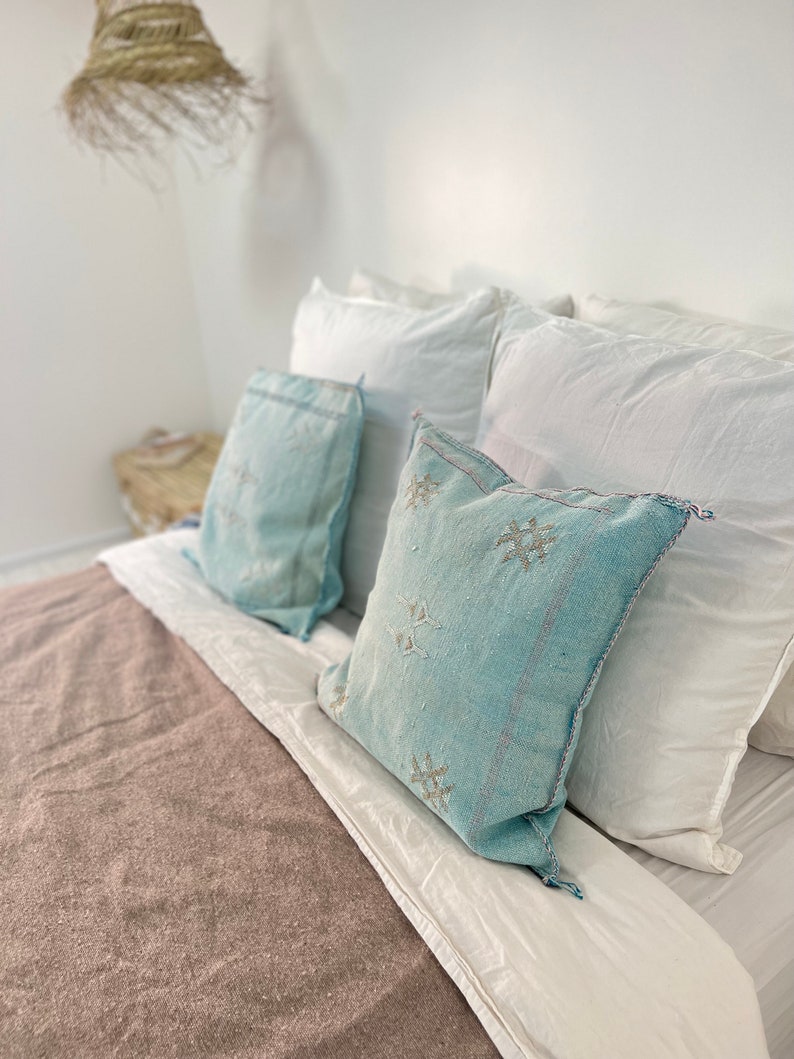 May include: A bed with a brown blanket and white pillows. Two blue patterned throw pillows are on top of the white pillows.