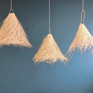 Peut inclure: Trois lampes suspendues en osier naturel suspendues au plafond contre un mur bleu. Les lampes sont faites de matériaux naturels et ont un style rustique et bohème.