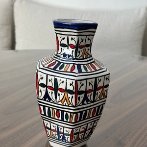 Op de afbeelding: Een witte keramische vaas met een geometrische vorm en kleurrijke Marokkaanse patronen in blauw, rood, geel en groen.