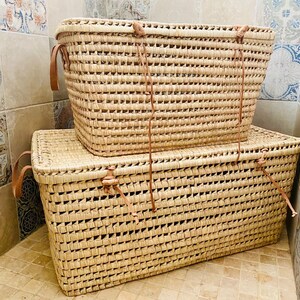 May include: Two woven seagrass storage baskets with leather handles. The larger basket is stacked on top of the smaller basket.