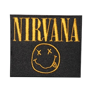 May include: A black and gold embroidered patch with the word "NIRVANA" in gold lettering and a yellow smiley face with two Xs for eyes.