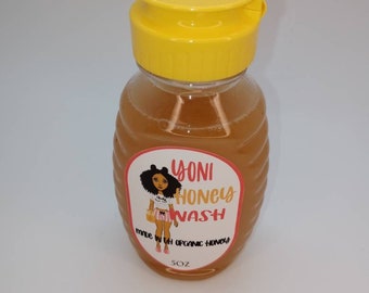 May include: A clear plastic bottle with a yellow flip top lid. The bottle contains a light yellow liquid and has a label with a cartoon illustration of a woman and the text "Yoni Honey Wash Made with Organic Honey 5oz".