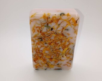 May include: A rectangular bar of soap with a pink base and flecks of dried yellow flowers throughout.