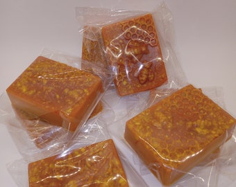 May include: Four bars of honey soap wrapped in clear plastic bags. The soap is a light orange color and has a honeycomb pattern embossed on the surface.