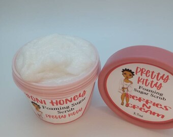 May include: Two pink jars with white lids. The jar on the left contains a white foaming sugar scrub. The jar on the right contains a white cream. Both jars have a pink and white label with the text "Pretty Kitty" and the text "Foaming Sugar Scrub" and "Berries N Cream".