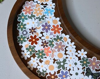 Peut inclure: Un plateau en bois en forme de demi-lune rempli d'autocollants de marguerites colorés. Les autocollants sont dans différentes nuances de rose, bleu, vert, jaune et orange. Il y a aussi un autocollant de papillon.