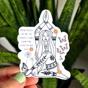 May include: A white sticker featuring a line drawing of a woman in a yoga pose, with long hair and intricate patterns on her clothing. The sticker includes the text "HOW SILLY OF ME TO FORGET THAT I AM THE LOVE OF MY LIFE" and decorative butterflies and flowers.