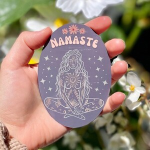 May include: A purple and white sticker with a woman sitting in a yoga pose. The sticker has the word "Namaste" written on it.