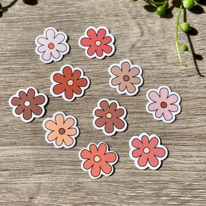 Peut inclure: Dix autocollants de fleurs dans diff&eacute;rentes nuances de rose, orange et marron. Les autocollants sont dispos&eacute;s en cercle sur une surface en bois.