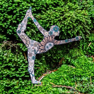 May include: A cutout of a person in a yoga pose, decorated with floral patterns, is placed on a bed of green moss.
