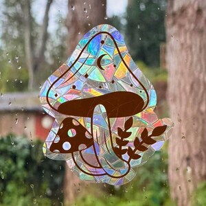 May include: A decorative window cling with a mushroom design. The large mushroom cap has a mosaic pattern with iridescent colours, a crescent moon, and stars. A smaller mushroom and leaves are also included.