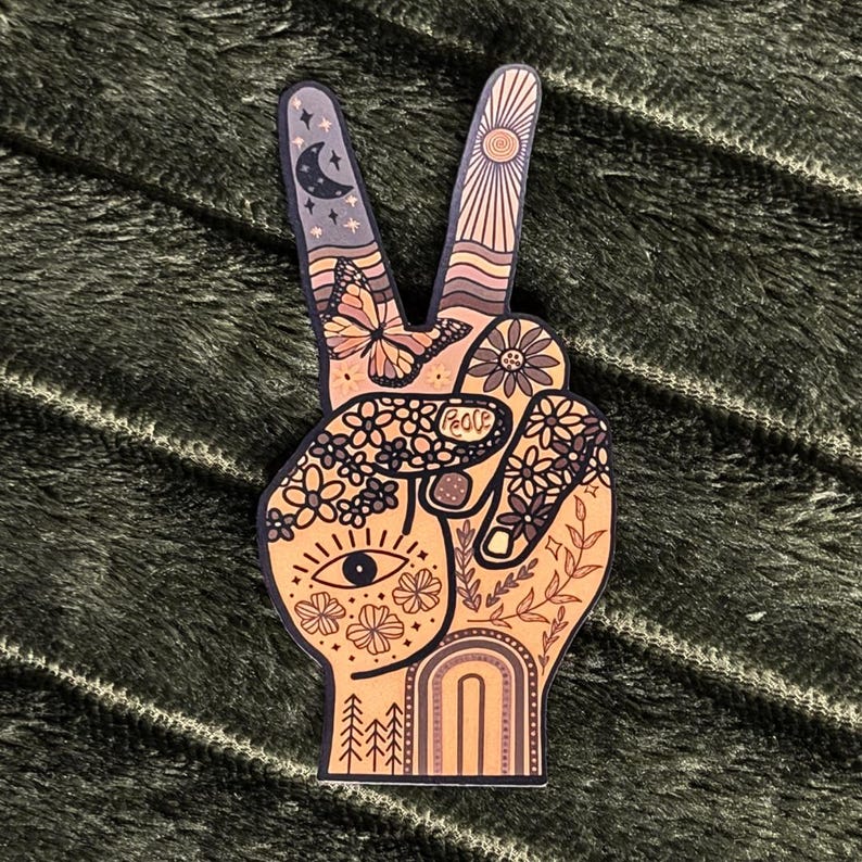 May include: A die-cut sticker shaped like a hand making a peace sign. The design features a warm color palette with illustrations of a butterfly, a crescent moon, stars, a sun, flowers, an eye, a rainbow, and trees. The word Peace is written.