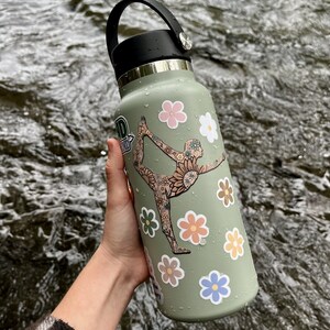 May include: A green reusable water bottle with a black lid and handle. The bottle is decorated with colorful flower and floral pattern stickers. One sticker features a woman doing a yoga pose.