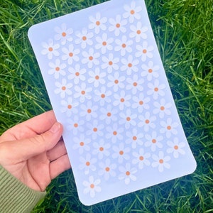 May include: A sheet of white sticker paper with a repeating pattern of white daisies with orange centres.