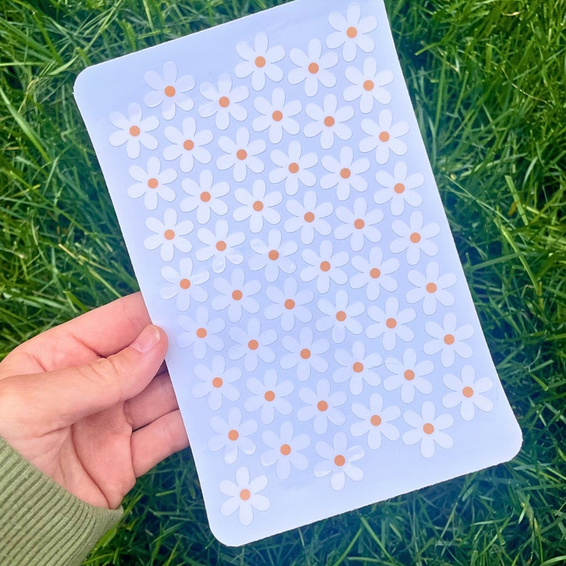 May include: A sheet of white sticker paper with a repeating pattern of white daisies with orange centres.