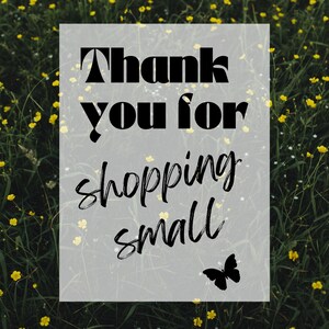 May include: A white sign with black text that reads "Thank you for shopping small" with a black butterfly silhouette in the bottom right corner. The sign is in front of a field of yellow wildflowers.