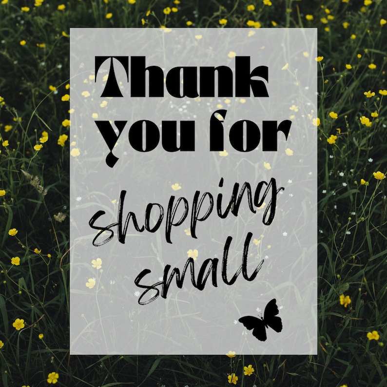 May include: A white sign with black text that reads "Thank you for shopping small" with a black butterfly silhouette in the bottom right corner. The sign is in front of a field of yellow wildflowers.