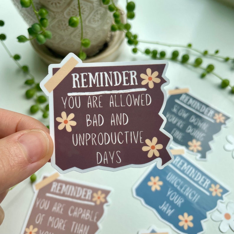 May include: Four brown, blue and grey stickers with white text and flower illustrations. The text on the brown sticker reads "Reminder: You are allowed bad and unproductive days".