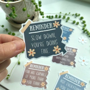 May include: A set of four motivational reminder stickers with a distressed paper look and floral accents. The stickers feature the text "Reminder" followed by a short message. The messages are: "Slow down, you're doing fine.", "You are capable of more than you think.", "Not everything you think is true." and "Back-to-back lowed and unproductive days."