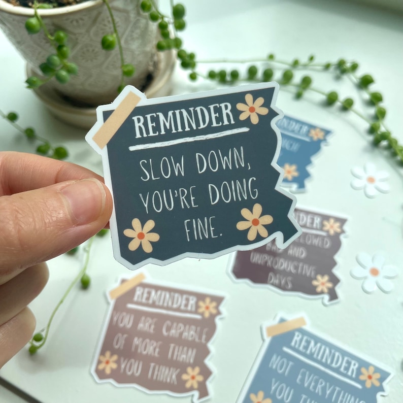 May include: A set of four motivational reminder stickers with a distressed paper look and floral accents. The stickers feature the text "Reminder" followed by a short message. The messages are: "Slow down, you're doing fine.", "You are capable of more than you think.", "Not everything you think is true." and "Back-to-back lowed and unproductive days."