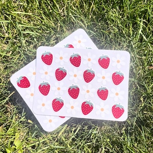 May include: A sheet of stickers with a white background and red strawberries and white flowers. The stickers are arranged in a repeating pattern.