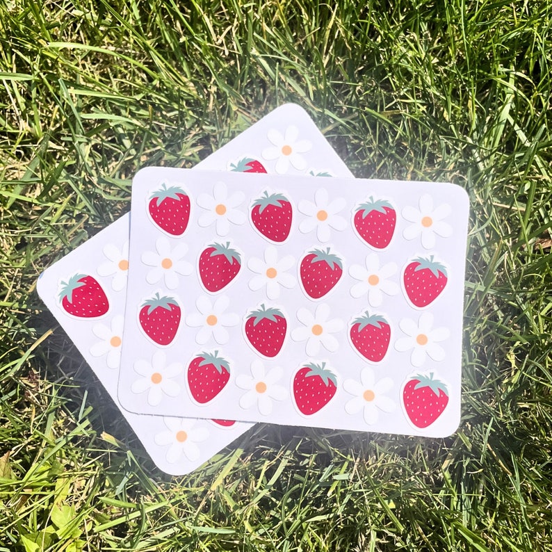 May include: A sheet of stickers with a white background and red strawberries and white flowers. The stickers are arranged in a repeating pattern.