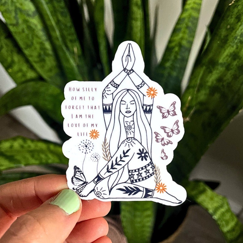 May include: A white sticker featuring a line drawing of a woman in a yoga pose, with long hair and intricate patterns on her clothing. The sticker includes the text "HOW SILLY OF ME TO FORGET THAT I AM THE LOVE OF MY LIFE" and decorative butterflies and flowers.