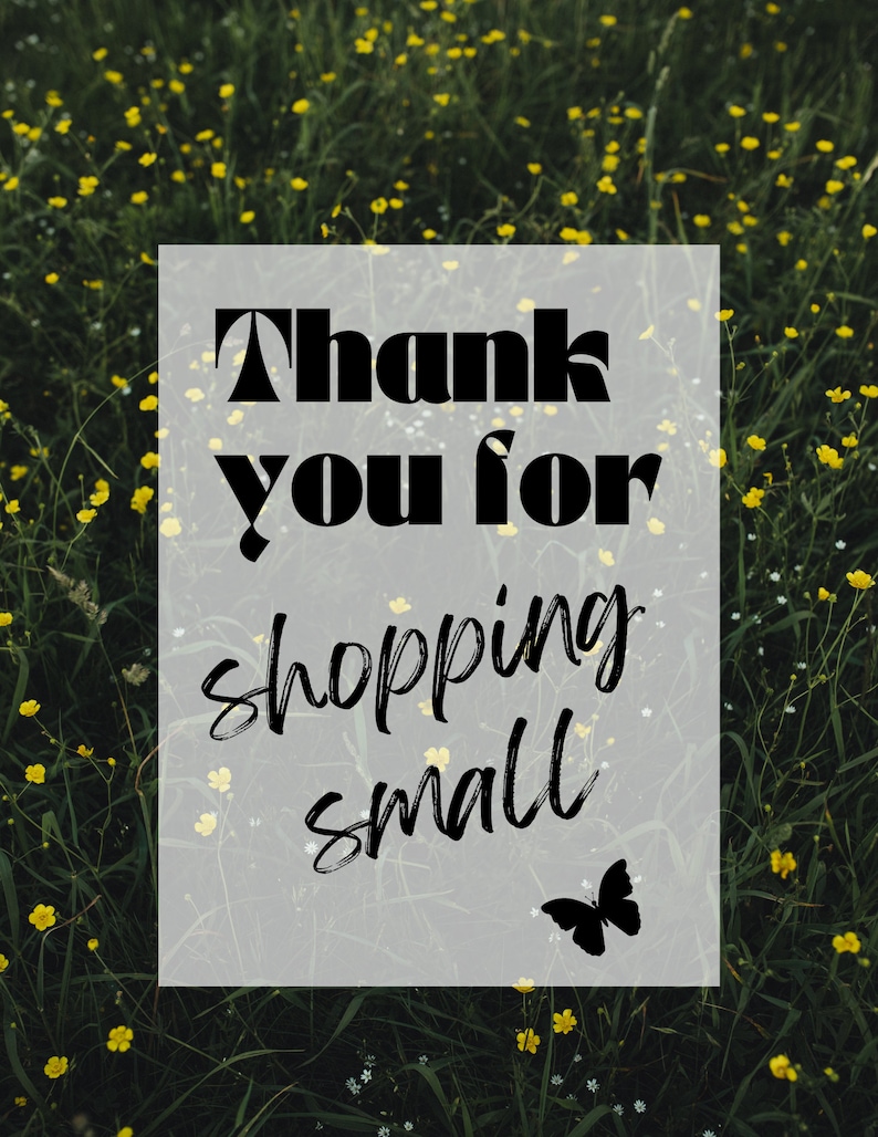 May include: A white sign with black text that reads "Thank you for shopping small" with a black butterfly silhouette in the bottom right corner. The sign is in front of a field of green grass and yellow flowers.
