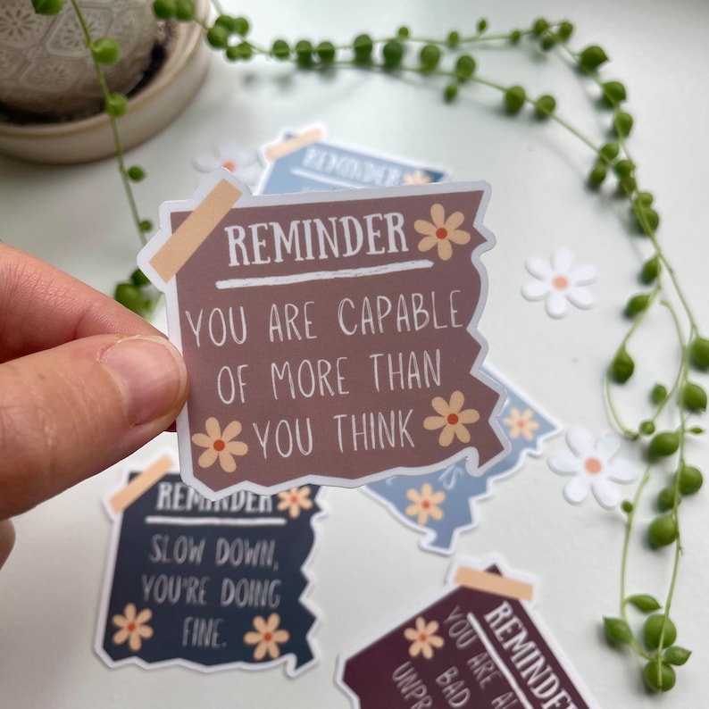 May include: A set of four motivational reminder stickers with a distressed paper look and floral accents. The stickers feature the text "Reminder" and positive affirmations. The text on the stickers reads: "You are capable of more than you think", "Slow down, you're doing fine", "You are all unpr", and "You are al bad".