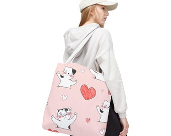 May include: Pink tote bag featuring a repeating pattern of cartoon cats and hearts. The cats are black and white with expressive faces, and the hearts are red. The bag has a white strap and is made of a soft material.